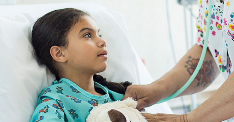 Young girl lying in hospital bed with a stuffed bear